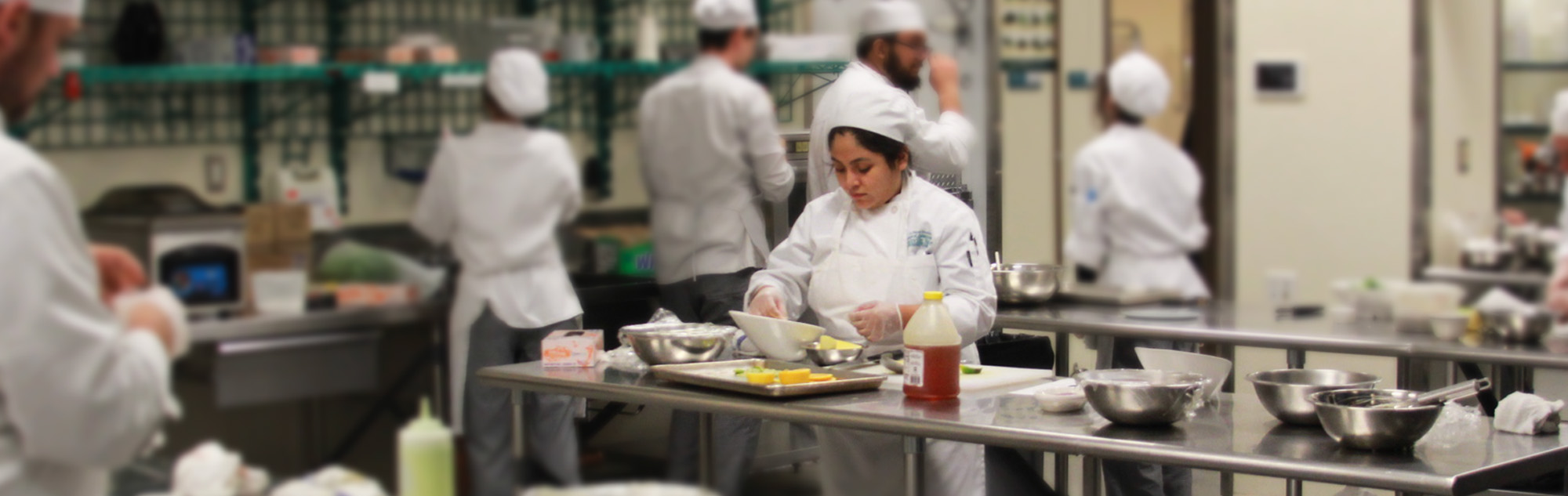 Culinary students prepare entrees in kitchen classroom.