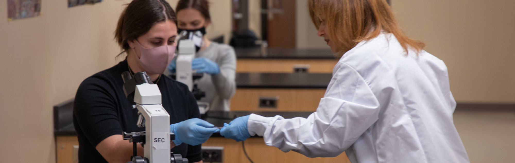 Student looks through microscope with assistance from professor.