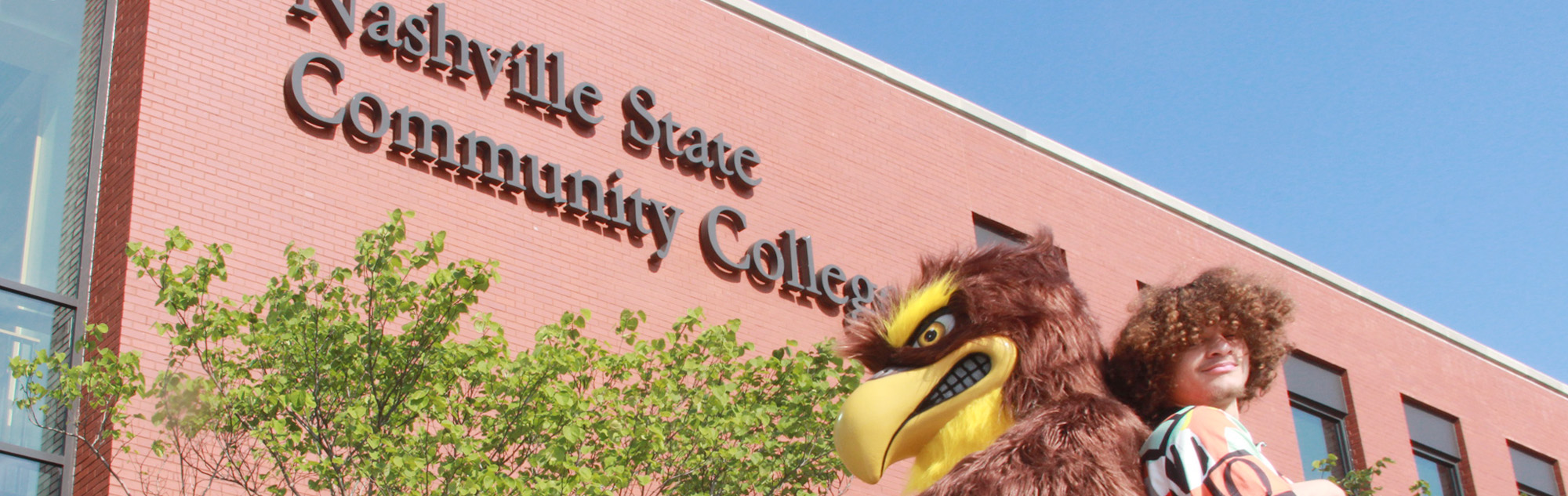 Student and mascot Finn stand in front of building.