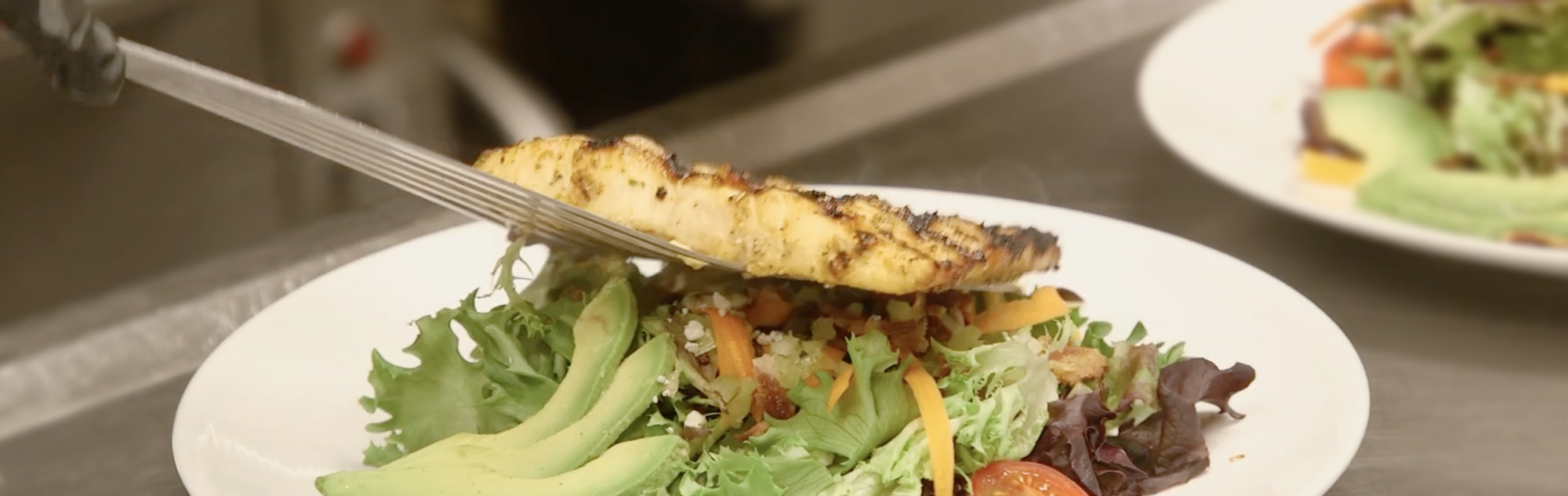 Grilled chicken is placed on green salad.